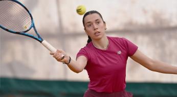 Giocatrice di tennis concentrata colpisce la palla su campo di terra rossa.