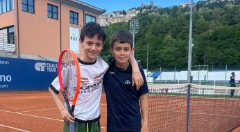 Due ragazzi felici su un campo da tennis, sorridono con le racchette in mano.